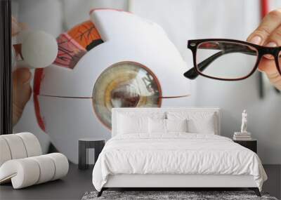 Optometrist woman holding glasses near anatomical model eye Wall mural