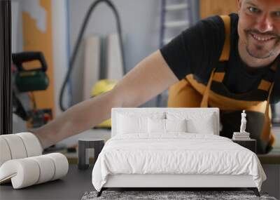 Portrait of smiling cheerful male installing wooden floor in new flat. Professional building worker. White gloves on hands. Construction site and renovation concept Wall mural