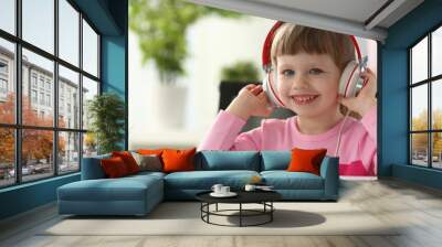 Portrait of smiling cute little girl wearing headphones while studying online at home . Education concept. Copy space Wall mural