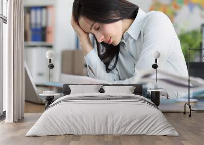 Tired exhausted young woman sits at laptop in office Wall mural