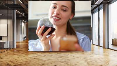 Young beautiful attractive girl drinks wine in the kitchen from a glass at breakfast time, spends her day off with alcohol write a message to a former boyfriend and smiles ex Wall mural