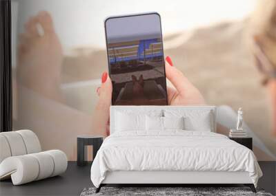 Young woman lying on sun lounger on beach and taking pictures of her feet on mobile phone closeup Wall mural