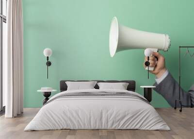 A hand in a sleek grey suit holding a modern white megaphone, with a mint green backdrop and subtle shadows Wall mural