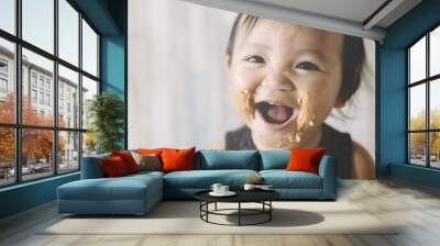 Asian Baby girl smiling with mouth and face full of peanut butter Wall mural