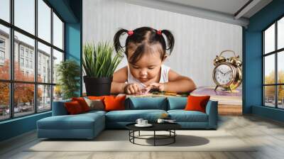 asian baby toddler reading book on wooden table with alarm clock. concept of early education, child learning and development Wall mural