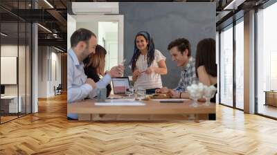 Smiling business woman standing in front of the table during presentation. Young woman standing in office and looking at co workers smiling Wall mural