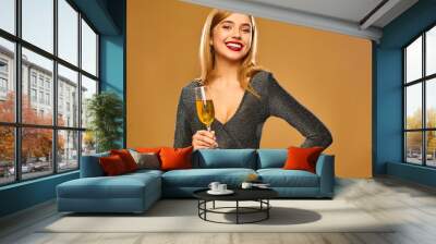 Beautiful blond woman celebrating New Year.Model having fun at fashion party.Happy smiling girl in stylish glamorous dress with champagne glass. Isolated on golden background Wall mural