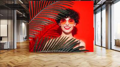 Fashion beauty portrait of young smiling brunette woman with evening stylish  makeup. Sexy model with curly short hair posing in studio. With red bright lips. Tropical palm leaf. In sunglasses Wall mural