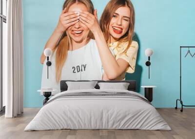 Girl surprising her female best friend. Model covering her eyes and hugging  from behind. Two surprised girls. Women having fun and showing face emotions Wall mural