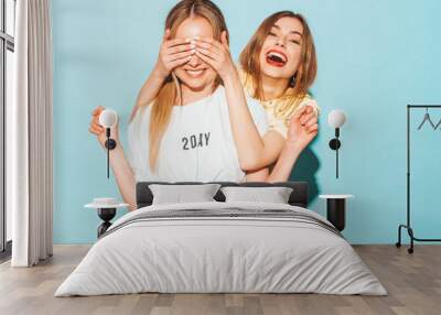 Girl surprising her female best friend. Model covering her eyes and hugging  from behind. Two surprised girls. Women having fun and showing face emotions Wall mural