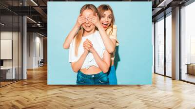 Girl surprising her female best friend. Model covering her eyes and hugging  from behind. Two surprised girls. Women having fun and showing face emotions Wall mural