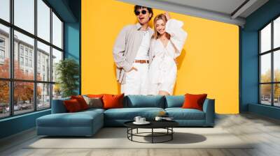 Happy beautiful romantic teenage couple. Smiling handsome caucasian man and young woman in summer clothes posing in studio, hugging sharing emotions, cheerful and happy. Isolated on yellow, sunglasses Wall mural