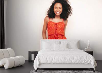 Portrait of beautiful black woman with afro curls hairstyle. Smiling model dressed in red summer dress. Sexy carefree female isolated white wall in studio Wall mural