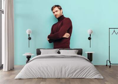 Portrait of handsome confident stylish hipster lambersexual model. Sexy man dressed in turtleneck sweater and trousers. Fashion male isolated on blue wall in studio Wall mural