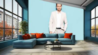 Portrait of handsome confident stylish hipster lambersexual model. Sexy modern man dressed in white elegant suit. Fashion male posing in studio near blue wall Wall mural