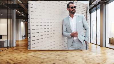 Portrait of handsome confident stylish hipster lambersexual model.Modern man dressed in elegant white suit. Fashion male posing in the street background near fence at sunset. In sunglasses Wall mural