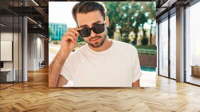 Portrait of handsome smiling stylish hipster lambersexual model.Man dressed in white T-shirt. Fashion male posing on the street background in sunglasses outdoors Wall mural