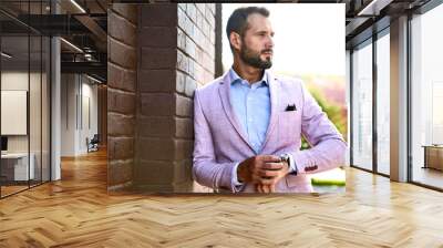 Portrait of sexy handsome fashion businessman model dressed in elegant suit posing near brick wall on the street background. Metrosexual Wall mural