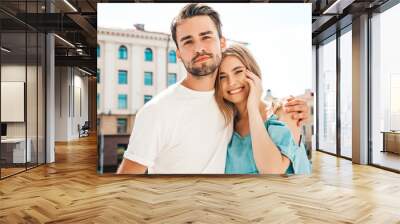 Portrait of smiling beautiful woman and her handsome boyfriend. Woman in casual summer jeans dress. Happy cheerful family. Female having fun. Couple posing on the street background Wall mural