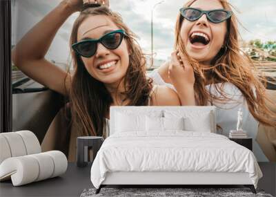 Portrait of two young beautiful and smiling hipster female in convertible car. Sexy carefree women driving cabriolet. Positive models riding and having fun in sunglasses outdoors.Enjoying summer days Wall mural