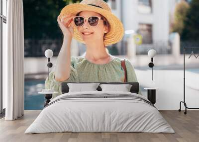 Portrait of young beautiful smiling brunette woman in trendy summer dress. Sexy carefree woman posing in street. Positive model outdoors at sunny day. Cheerful and happy.  In hat and sunglasses Wall mural