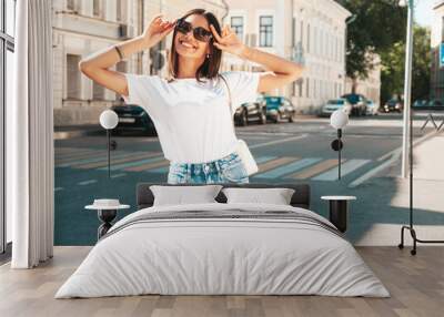 Portrait of young beautiful smiling hipster woman in trendy summer jeans shorts. Sexy carefree model posing on the street background at sunset. Positive model outdoors im sunglasses Wall mural