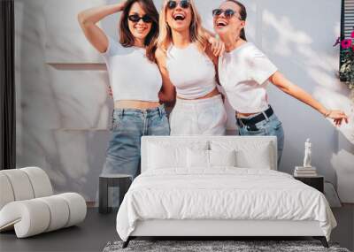 Three young beautiful smiling hipster female in trendy summer white t-shirt  and jeans clothes. Sexy carefree women posing in street. Positive models having fun, going crazy. In sunny day, sunglasses Wall mural