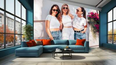 Three young beautiful smiling hipster female in trendy summer white t-shirt  and jeans clothes. Sexy carefree women posing in street. Positive models having fun, going crazy. In sunny day, sunglasses Wall mural