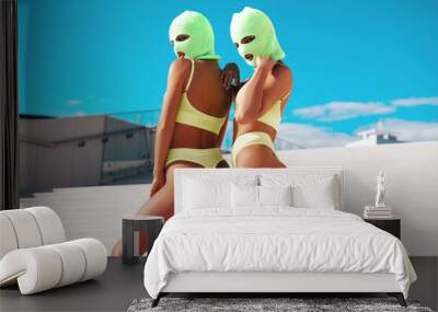 Two beautiful sexy women in green underwear. Models wearing bandit balaclava mask. Hot seductive female in nice lingerie posing in the street at sunny day, blue sky. Crime and violence. Perfect body Wall mural