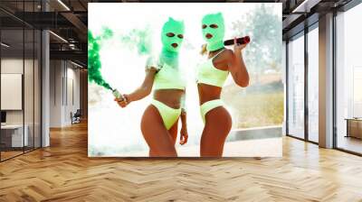 Two beautiful sexy women in green underwear. Models wearing bandit balaclava mask. Hot seductive female in nice lingerie posing in the street at sunny day. Crime and violence. Hold smoke bomb Wall mural