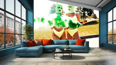 Two beautiful sexy women in green underwear. Models wearing bandit balaclava mask. Hot seductive female in nice lingerie posing in the street at sunny day. Crime and violence. Hold yellow smoke bomb Wall mural