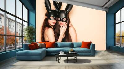 Two sexy beautiful women wearing carnival black mask of Easter bunny rabbit.Hot brunette girls posing near wall in studio. Seductive models in nice lingerie Wall mural