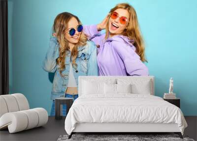 Two young beautiful blond smiling hipster girls in trendy summer clothes. Sexy carefree women posing near blue wall in sunglasses. Positive models going crazy Wall mural