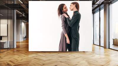 Two young beautiful brunette girls in nice trendy summer suit clothes.Sexy carefree women posing near white wall in studio.Fashionable models with bright evening makeup.They hug and touch each other Wall mural