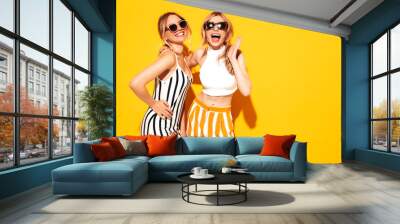 Two young beautiful smiling blond hipster female in trendy summer clothes. Sexy carefree women posing near yellow wall in studio. Positive models having fun. Cheerful and happy. In sunglasses Wall mural