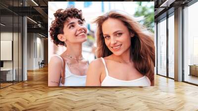 Two young beautiful smiling hipster female in trendy summer white t-shirt and shorts clothes. Sexy carefree women posing in the street. Positive models having fun, hugging and going crazy, closeup Wall mural