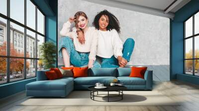 Two young beautiful smiling international hipster female in trendy summer jeans clothes. Sexy carefree women posing near gray wall in studio. Positive models having fun. Concept of friendship Wall mural