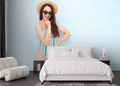 Young beautiful sexy smiling  hipster woman in posing near light blue wall in studio. Trendy model in colorful summer swimwear bathing suit. Positive model going crazy.Happy and cheerful in hat Wall mural