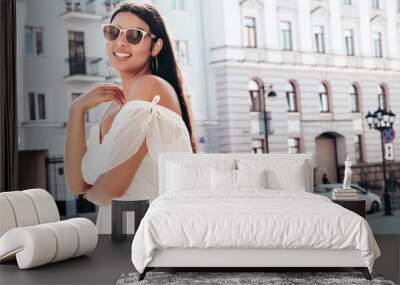 Young beautiful smiling hipster woman in white dress. Sexy carefree model posing on the street background at sunset. Positive female outdoors at warm sunny day. Cheerful and happy. In sunglasses Wall mural