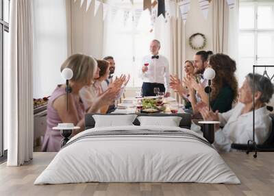 A big family sitting at a table on a indoor birthday party, a senior man giving a speech. Wall mural