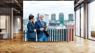 A businessman and businesswoman with diary standing on a terrace, working. Wall mural