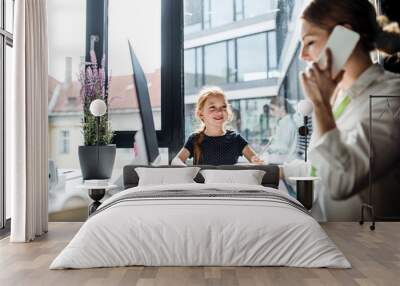 A businesswoman with small daughter sitting in an office, working. Wall mural