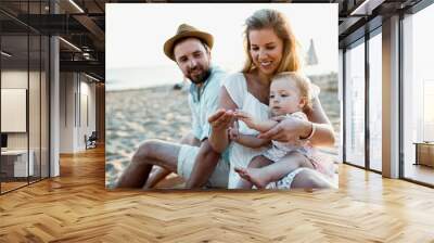 A family with a toddler girl sitting on sand beach on summer holiday. Wall mural