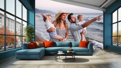 A family with two toddler children walking on beach on summer holiday at sunset. Wall mural