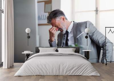 A frustrated businessman sitting at the desk in an office, hearing bad news. Wall mural