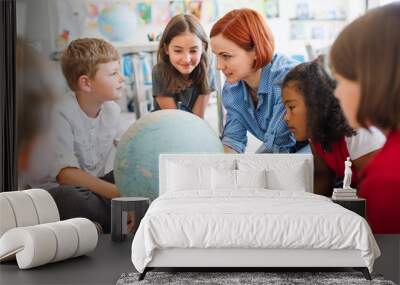 A group of small school kids with teacher sitting on the floor in class, learning. Wall mural