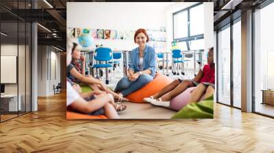 A group of small school kids with teacher sitting on the floor in class, talking. Wall mural