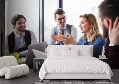 A group of young business people with laptop sitting in an office, talking. Wall mural