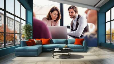 A group of young business people with laptop sitting in an office, talking. Wall mural