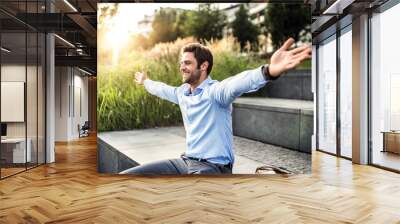 A happy young businessman with arms stretched outdoors at sunset. Wall mural